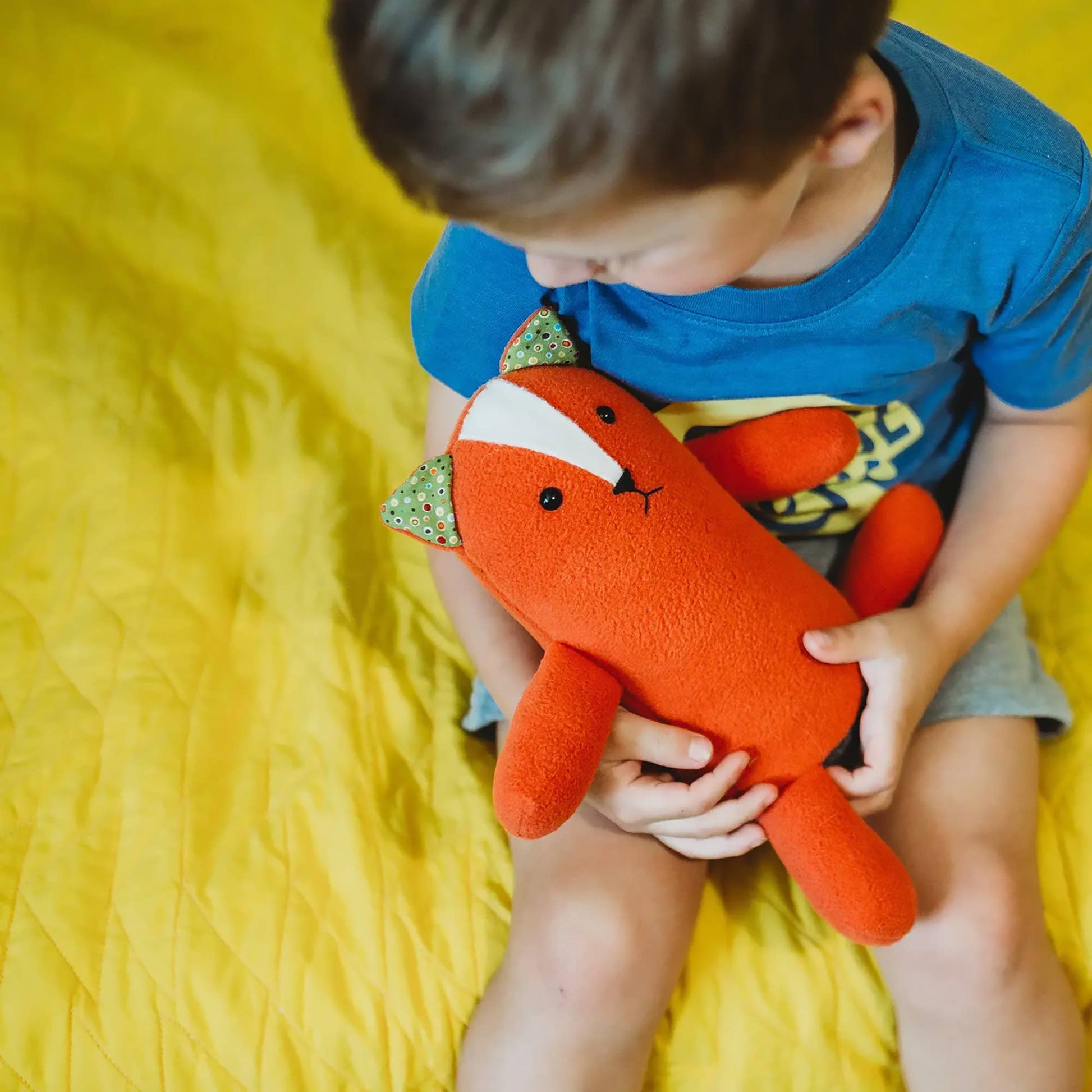 Child holding a red fox plush toy on a yellow blanket