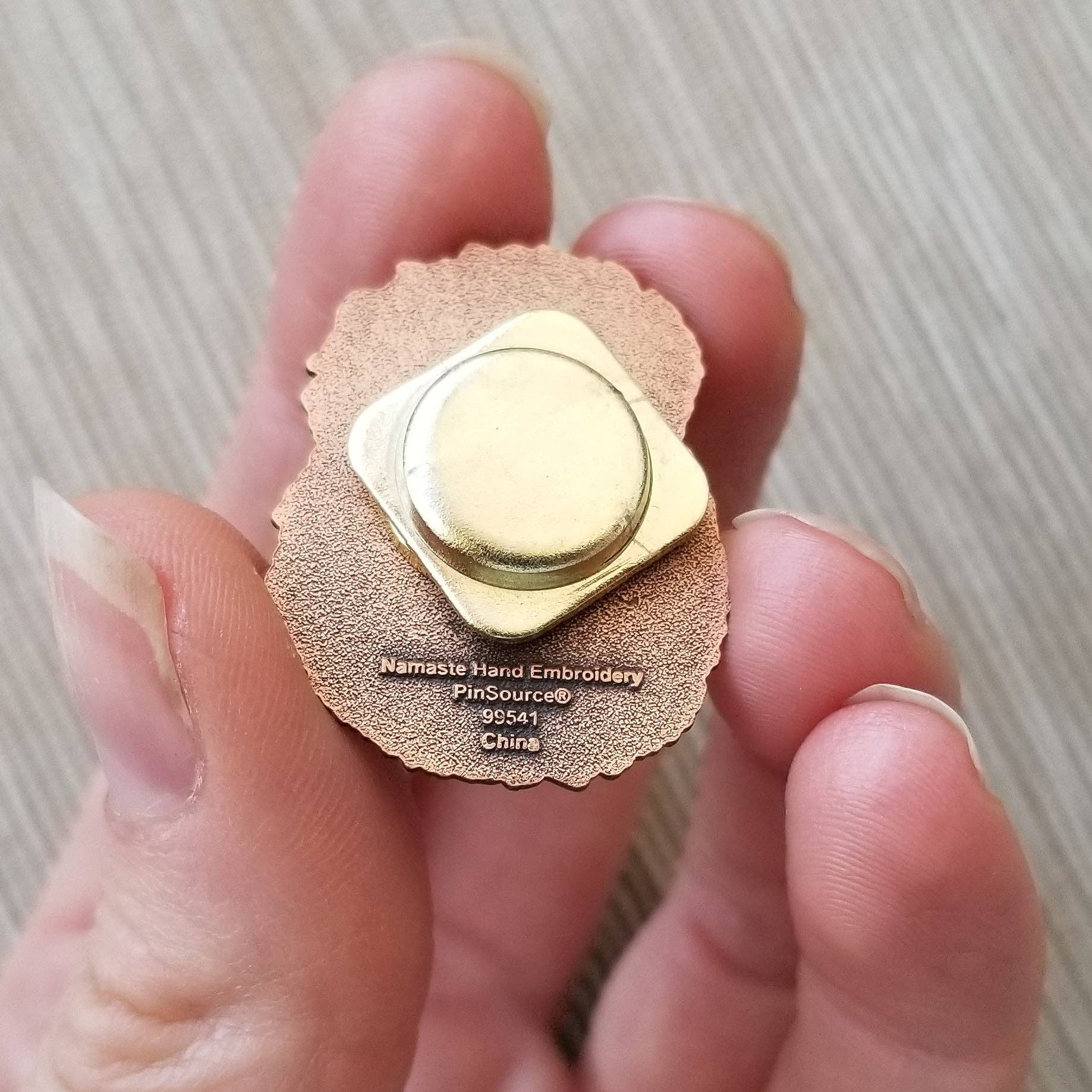 Gold fidget spinner held between fingers with 'Nanste Hand Embroidery' branding.